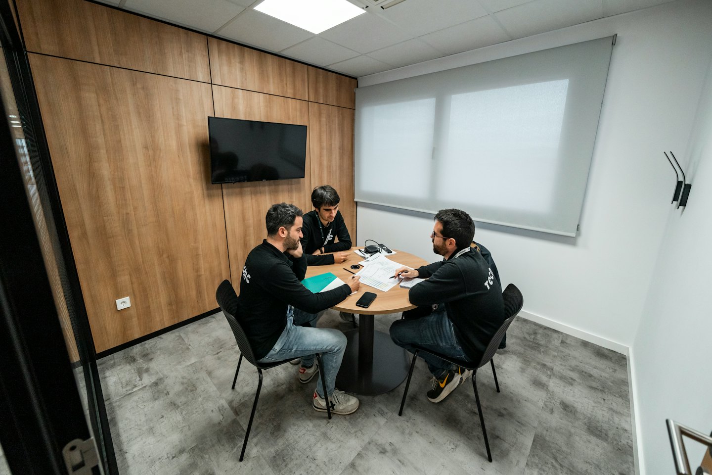 Tres profesionales discuten documentos en una pequeña mesa de reuniones.